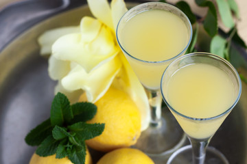Fototapeta na wymiar Limoncello in elegant liquor glasses with lemons, mint and yellow rose on steel plate. Sicilian lemon liquor aromatic and refreshing. Top view
