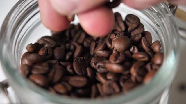 Close up jar full od brown coffee beans. grabbing coffee beans.
