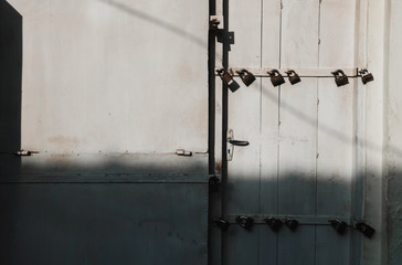 Old metal locks on a wooden door with deep shadows from the sun. Many locks on the door.