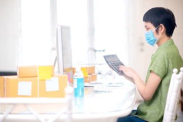 Fototapeta na wymiar Successful Asian on line business woman wearing surgical mask and sanitizer gel. Work from home during quarantine period of pandemic corona virus or covid-19