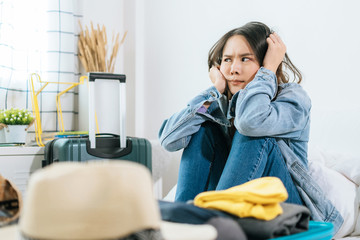 young asian pretty woman hipster traveler sad after flight cancelled with packing clothes into suitcase for holiday vacation on bed at home, delayed flight, summer holiday, backpacker, travel concept