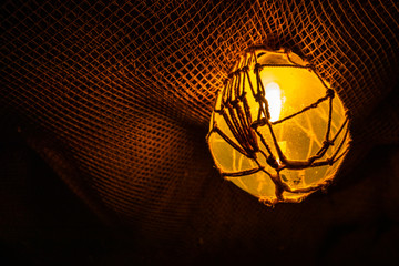 A yellow light casts a warm glow onto the texture of a fishing net hanging from the ceiling.