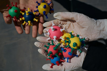 some gloved and some ungloved hands hold models of coronavirus.