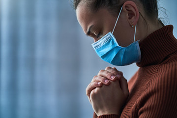 Woman in protective mask with closed eyes and praying hands, asks god for healing and recovery...