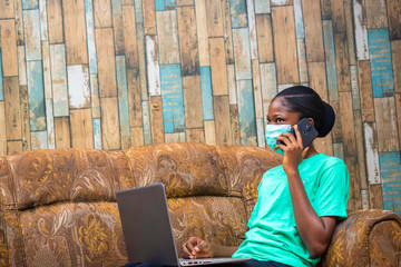 young black beautiful lady working on her laptop and wearing a nose mask to prevent her from a...