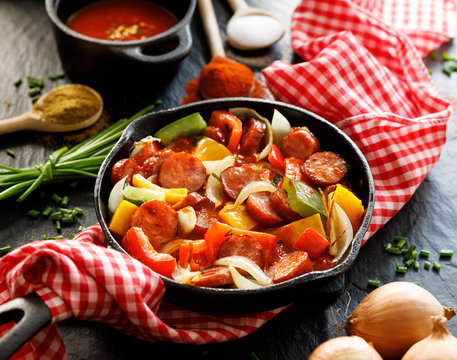 Stew with peppers, tomatoes and sausage in a cast iron skillet on a black background, close up Traditional Hungarian dish called lecho