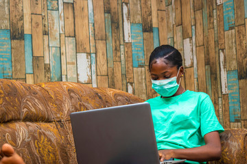 young black beautiful lady working on her laptop and wearing a nose mask to prevent her from a...