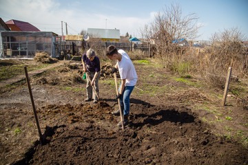 An elderly and a young man working on a farm, digging the ground