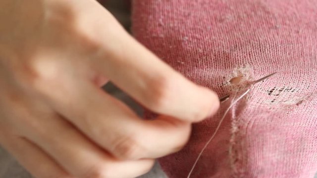  Woman sews up holes in pink socks. Handmade sewing. Poverty and beggary concept. 