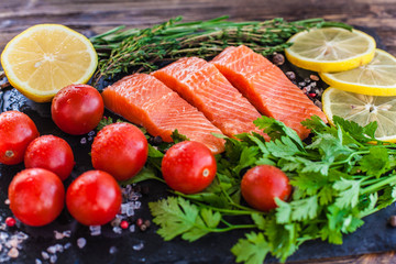 Three salmon steakes with greenery, lemon and cherry tomatoes on the black board