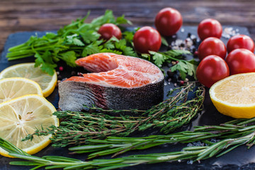 Fototapeta na wymiar a salmon steak with greenery, lemon and cherry tomatoes on the black board