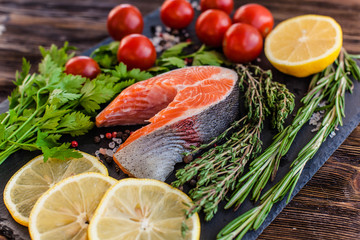 One salmon steak with greenery, lemon and cherry tomatoes on the black board