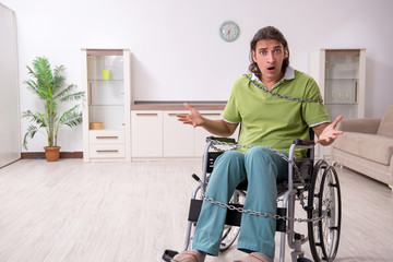 Young male invalid in wheel-chair suffering at home