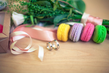 wedding rings on a table with macarons and a bouquet of flowers