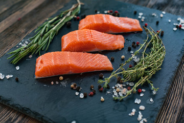 Three salmon steakes with thyme, rosemary, pepper and salt grains on the black board