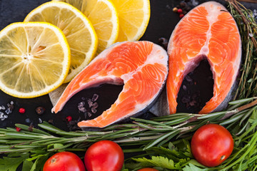 Two salmon steakes with greenery, lemon and cherry tomatoes on the black board