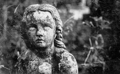 Dirty and retro styled image of an ancient stone statue of sad little angel with broken wings praying as symbol of sorrow, sadness, death and pain.