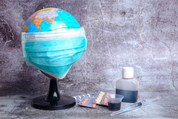 Globe wearing mask with medicines on crack wall background. Earth is combating corona virus. Malay word at the medicine mentioned shake well before you drink.