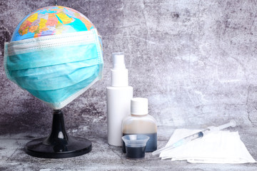 Globe wearing mask with medicine, injection syringe and extra face mask on crack wall background. Earth is combating corona virus. Malay word at the medicine mentioned shake well before you drink.