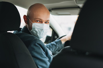 Fototapeta na wymiar Bald man taxi driver in medical face mask inside yellow car looks at camera, concept of coronavirus quarantine