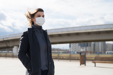 Fashionable stylish scared woman in protective blue face mask, gray wool coat on the street near metro station. Windy day. Self protection in transport during quarantine from coronavirus covid-2019