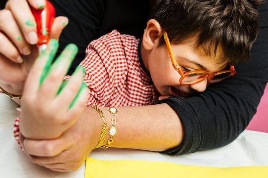 profesora educaci&oacute;n especial y alumno con bata est&aacute;n pintando con las manos una corona de cumplea&ntilde;os y una cartulina amarilla con pinturas acrilicas sobre la mesa. terapia de manualidades pl&aacute;sticas.