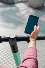 Person in the street riding an electric scooter and using a mobile phone. Rent a scooter with a smartphone app.