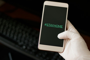 Hashtag stay home! The inscription on the smartphone screen. Female hand in a white glove holds a phone. The recommendation is quarantined at home to prevent coronovirus covid 19.