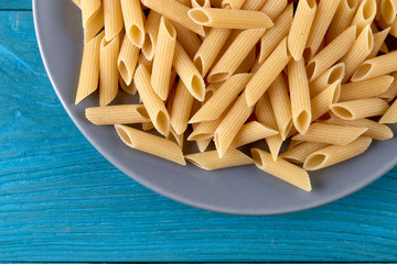 A lot of raw pasta penne on a plate at blue wooden background horizontal