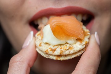 Closeup of a woman biting crackers with salmon and cream cheese under the lights