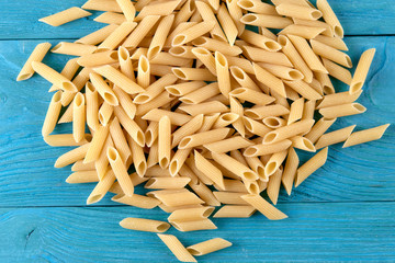 A lot of raw pasta penne on blue wooden background horizontal