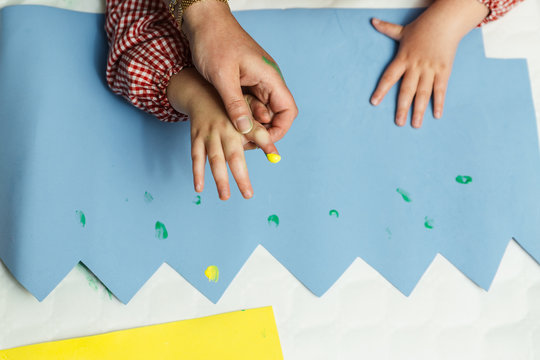 profesora educaci&oacute;n especial y alumno con bata est&aacute;n pintando con las manos una corona de cumplea&ntilde;os y una cartulina amarilla con pinturas acrilicas sobre la mesa. terapia de manualidades pl&aacute;sticas.