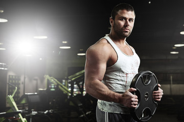 Fototapeta na wymiar Portrait of muscular strong athletic man pumping up muscles in the gym, brutal bodybuilder workout
