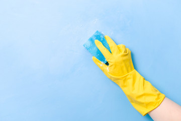a hand in a yellow rubber glove washes a wall with a wet foamy blue sponge, foam blue background...