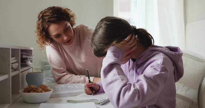 Caring young parent mom supporting tired upset teen school child daughter having difficulty with education learning at home. Mum comforting sad teenage girl encouraging helping with studies concept.