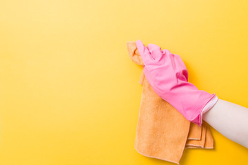 hand in a pink rubber glove holds an orange rag for washing and cleaning, yellow background copy...