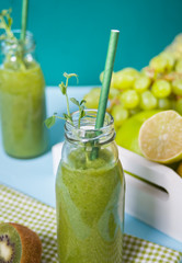 Fresh blended green smoothie in glass small bottles with fruit and vegetables on the background. Health and detox concept.