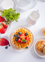 Plate with sweet tasty waffles with honey, berries, cup of tea on the white background.