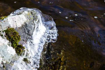 Beautiful spring landscape with water, ice and stone. Ice on a rock on sunny day. Melting snow sparkles in the sun. The ripples on the water. Nature concept. Environmental conservation concept.