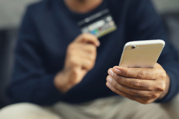 young male hands holding credit card and using phone sit order products on sofa using at home and search information Online shopping purchase Sell or Payment. filler vintage.	