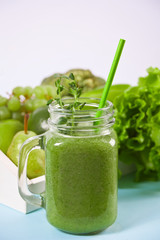 Fresh blended green smoothie in glass jar with fruit and vegetables on the background. Health and detox concept.