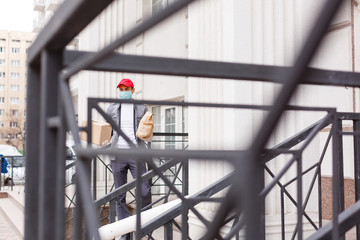 Courier in protective mask and medical gloves delivers takeaway food. Delivery service under quarantine, disease outbreak, coronavirus covid-19 pandemic conditions.