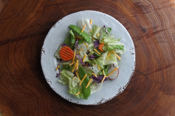 Mixed vegetable salad on a white plate with a background of tree rings