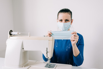 Woman hands using the sewing machine to sew the face home made diy medical mask during the coronavirus pandemia.