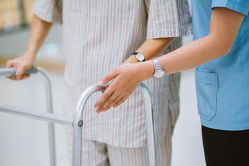 close up young physical therapist helping senior patient in using walker during rehabilitation