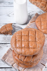 Stack of round brown rye flatbread against the white wooden background. Bottle of milk in the background