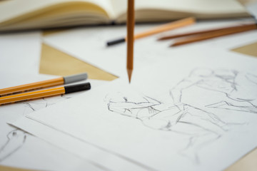 A top view flat lay of many figure drawing pencil and marker sketches. The artist worskspace with male and female drawings and pencils on the white paper, art, craft, creativity, inspiration, concepts