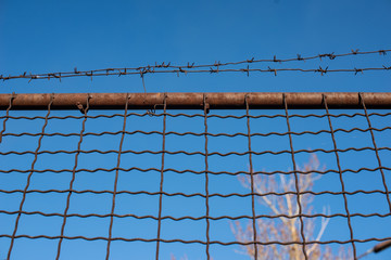 Fence with barbed wire on a background of blue clear sky.