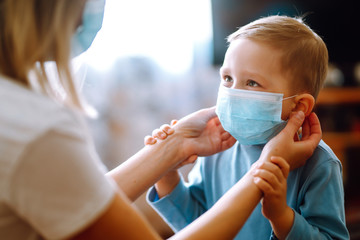 Little boy and mom in medical mask. Mother puts on her baby sterile medical mask. Child, wearing...