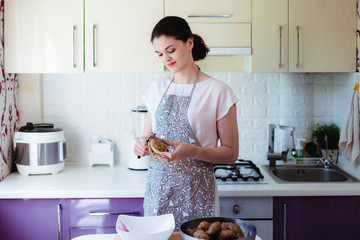 Young woman in kitchen in apron peeling potatoes